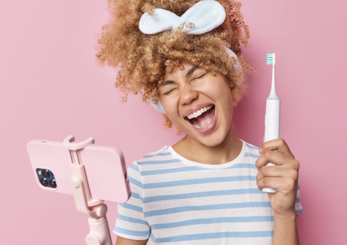 Chica en fondo rosa con cepillo de dientes y movil